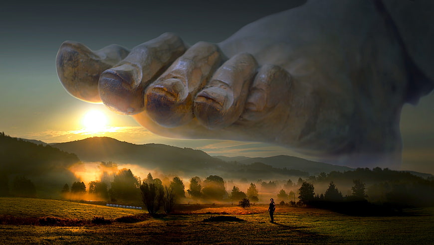 Surreal giant foot hovering over misty landscape at sunrise