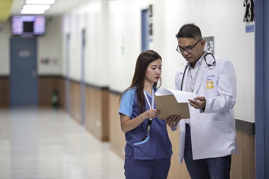 Doctor and Nurse Reviewing Medical Chart in Hospital Corridor