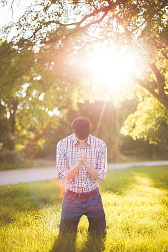 Man kneeling in prayer on grass with sun flare