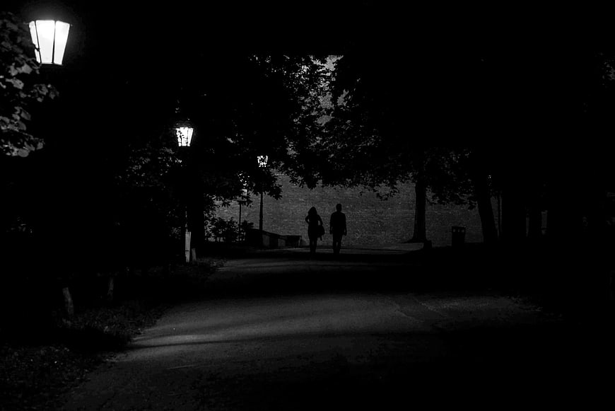 Silhouette of couple walking on dark park path at night