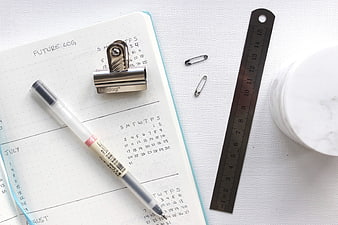 Flat lay of bullet journal, pen, ruler, and safety pins on white background