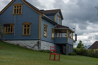 Blue wooden house with red chair on grassy hill