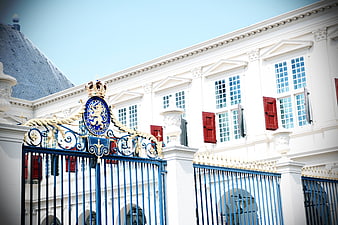 Ornate blue and gold gate of a white palace with red shutters