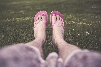Relaxed feet in pink flip flops on green grass