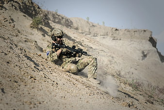 Soldier sliding down dusty hillside with rifle