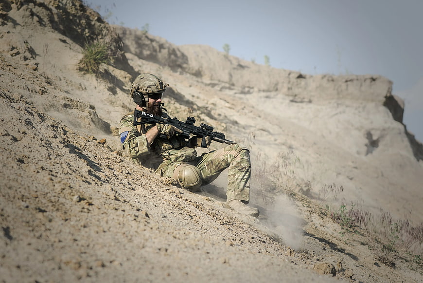 Soldier sliding down dusty hillside with rifle