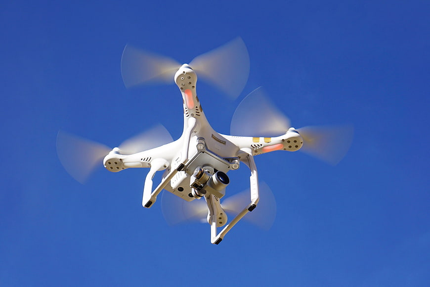 White DJI Phantom Drone Flying Against Clear Blue Sky