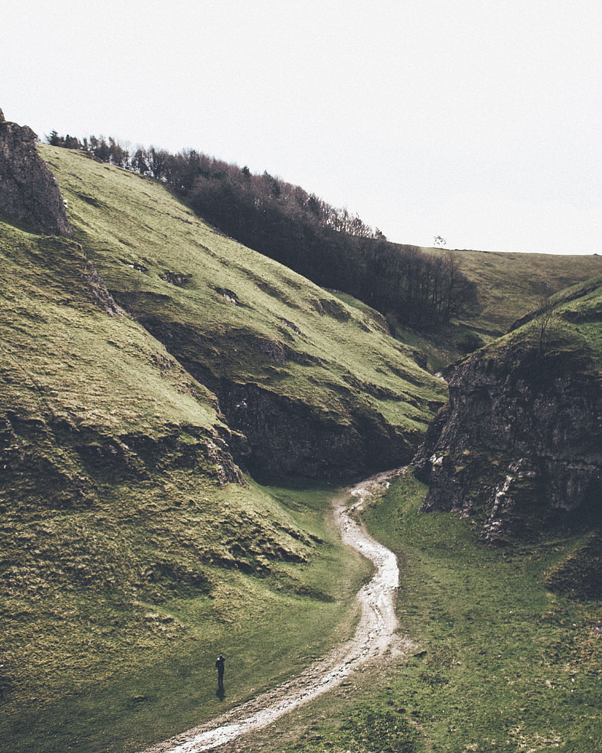 Lone Hiker Walking on Winding Path Through Green Highland Valley