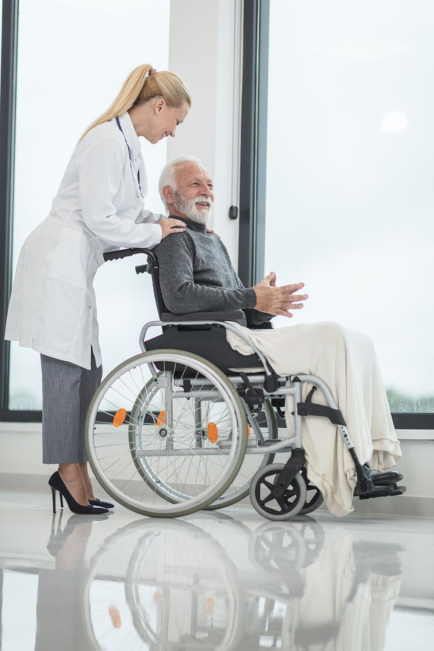 Female doctor comforting elderly male patient in wheelchair