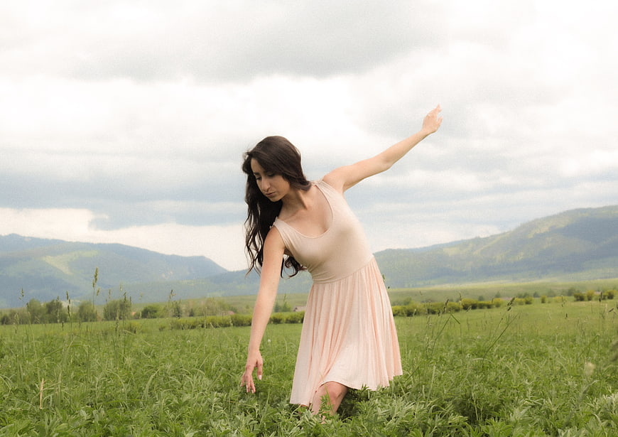 Woman in beige dress dancing in green meadow