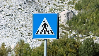 Blue pedestrian crossing sign against rocky mountain background