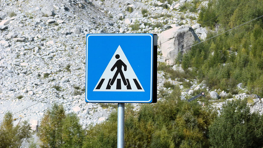 Blue pedestrian crossing sign against rocky mountain background