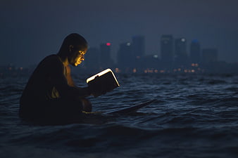 Man Reading Book in Ocean at Night with City Skyline