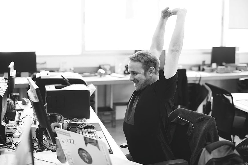 Happy Man Stretching Arms in Modern Office Workspace