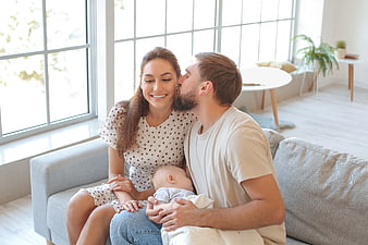 Happy young parents kissing baby on sofa at home