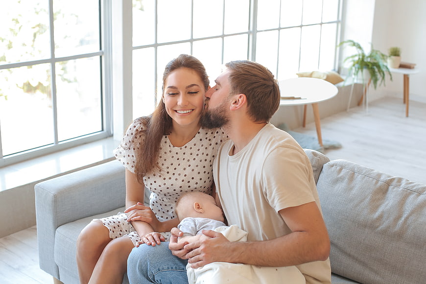 Happy young parents kissing baby on sofa at home