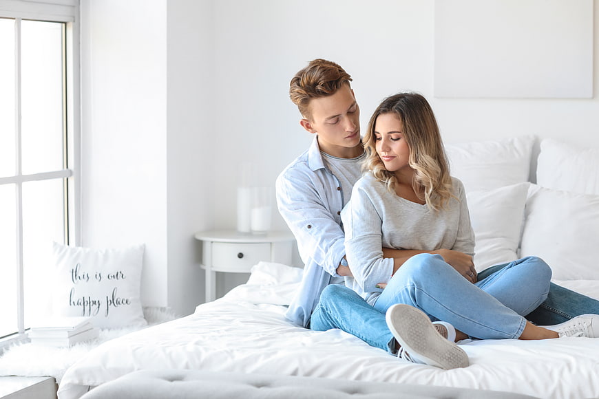 Happy couple hugging on bed in bright bedroom