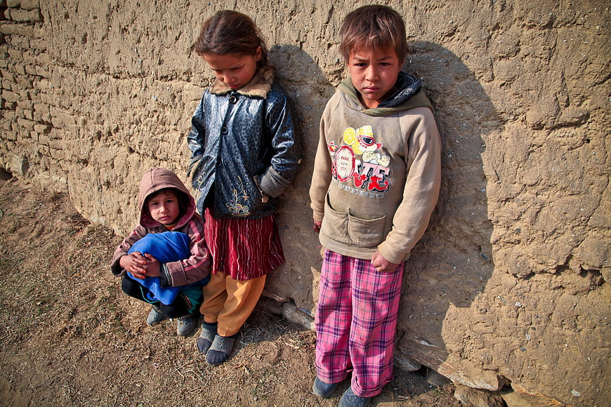 Three young children standing against a textured mud wall outdoors