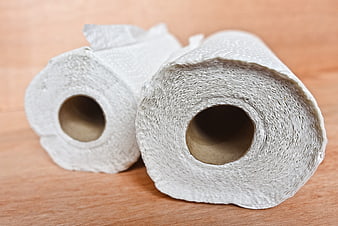 Two rolls of white paper towels on a wooden table