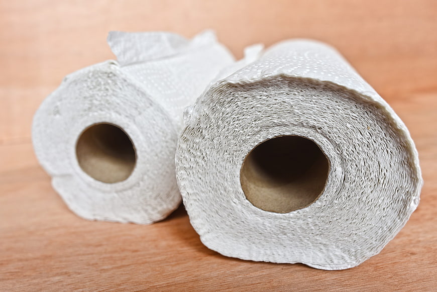 Two rolls of white paper towels on a wooden table