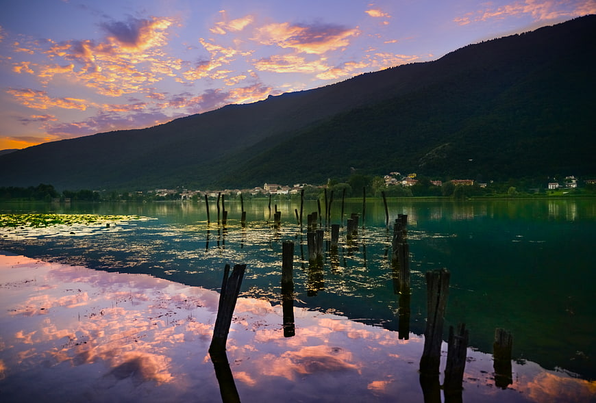 Serene lake sunset with wooden posts and mountain reflection