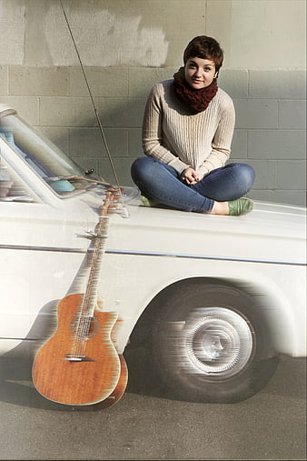 Woman sitting on vintage car with guitar motion blur