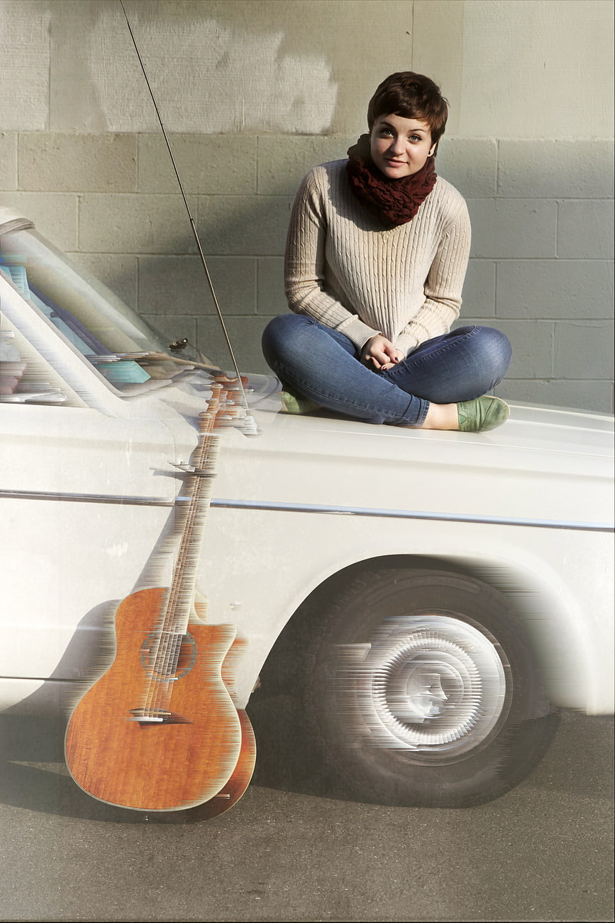 Woman sitting on vintage car with guitar motion blur