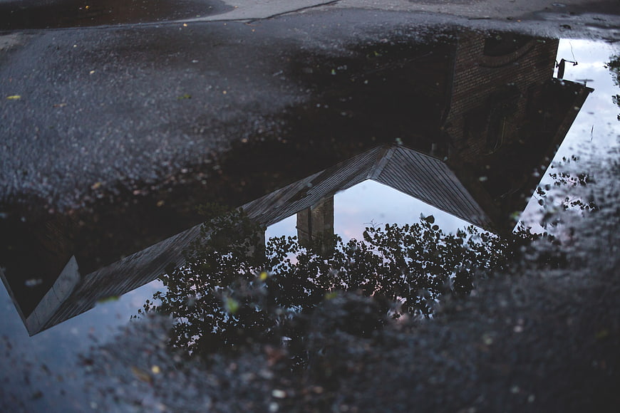 Moody Reflection of House and Trees in Rain Puddle