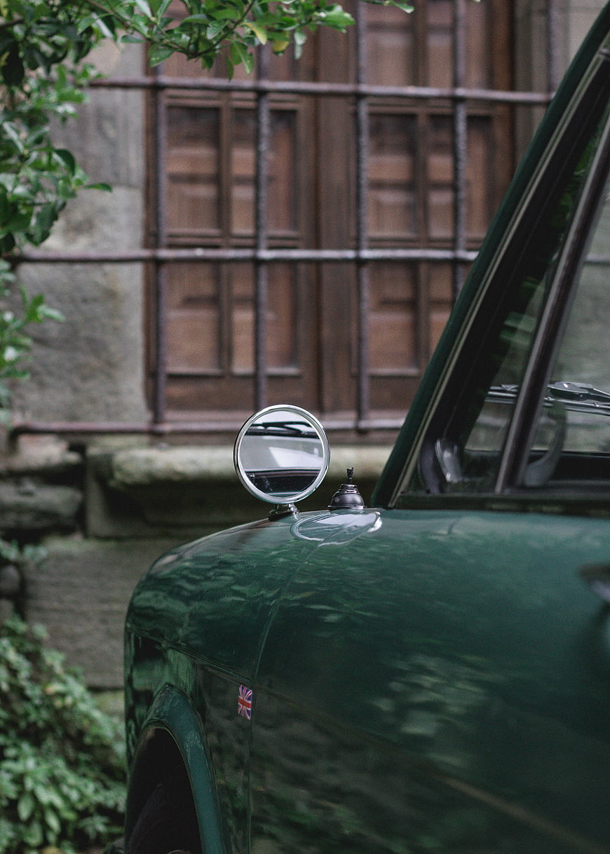 Close-up of vintage green car side mirror and hood