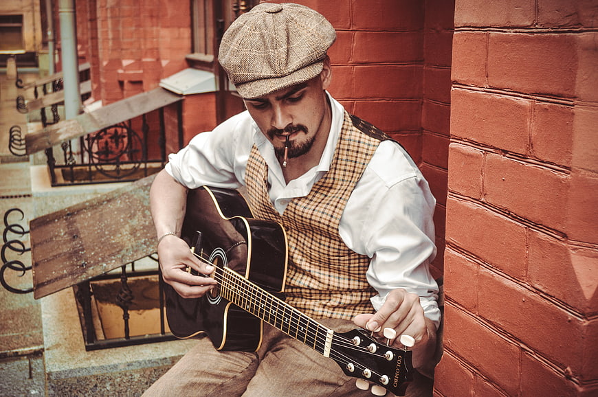 Vintage Man Playing Acoustic Guitar Against Red Brick Wall
