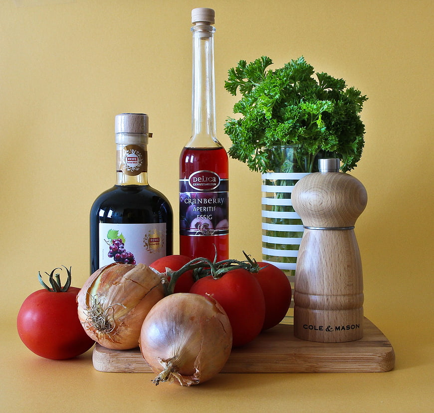 Still life of tomatoes, onions, vinegar, and parsley on a wooden board