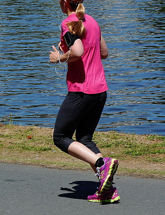 Woman jogging by lake wearing pink athletic gear