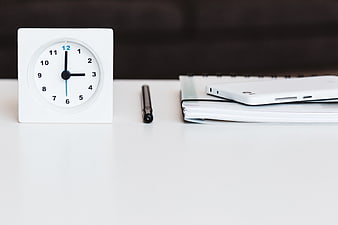 Minimalist white desk with clock, pen, notebook, and smartphone