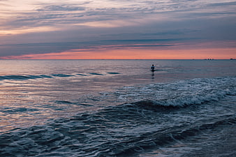 Lone fisherman in ocean waves during pink sunset