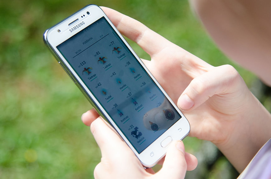 Hands Holding White Samsung Smartphone Playing Pokemon Go Outdoors