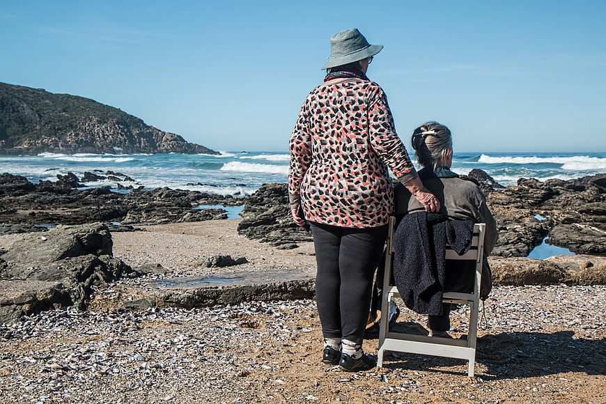 Senior Woman Supporting Elderly Woman on Beach Chair