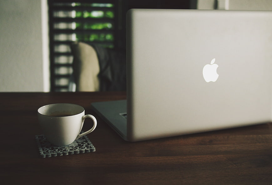 Silver laptop and coffee cup on wooden desk