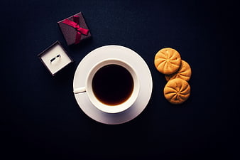 Flat lay of coffee, cookies, and engagement ring on dark background