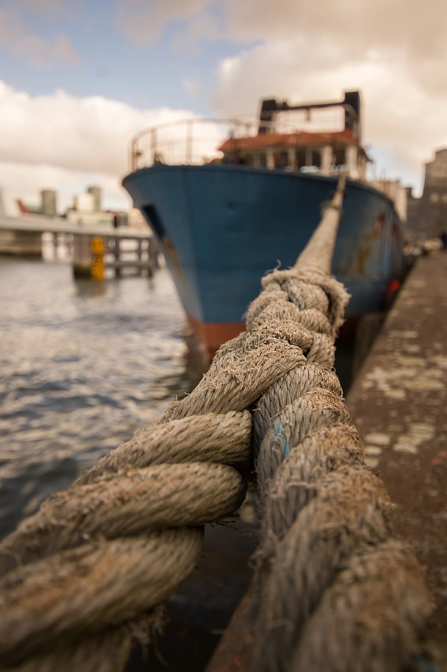Close-up of thick rope leading to blue boat at harbor