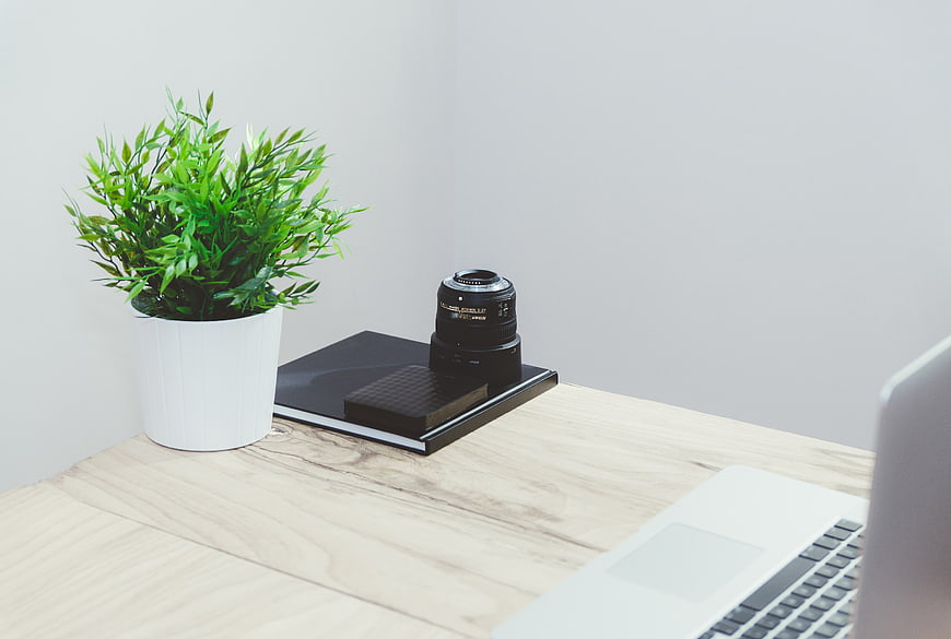 Minimalist workspace with laptop, camera lens, and plant