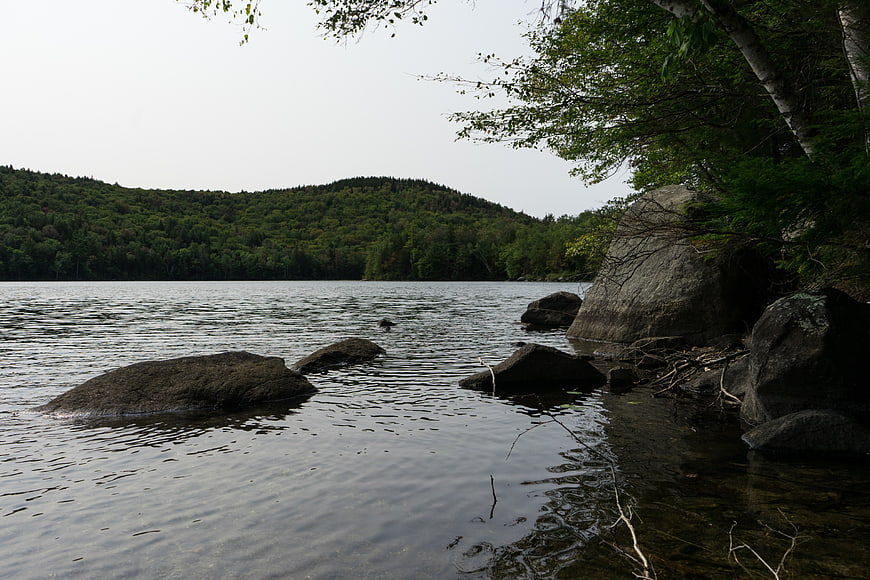 Serene Lake Shoreline with Rocks and Forested Hills