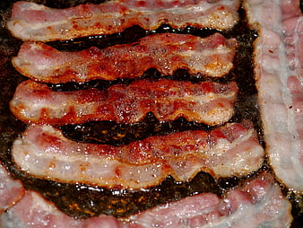 Close-up of raw bacon strips sizzling in a dark frying pan