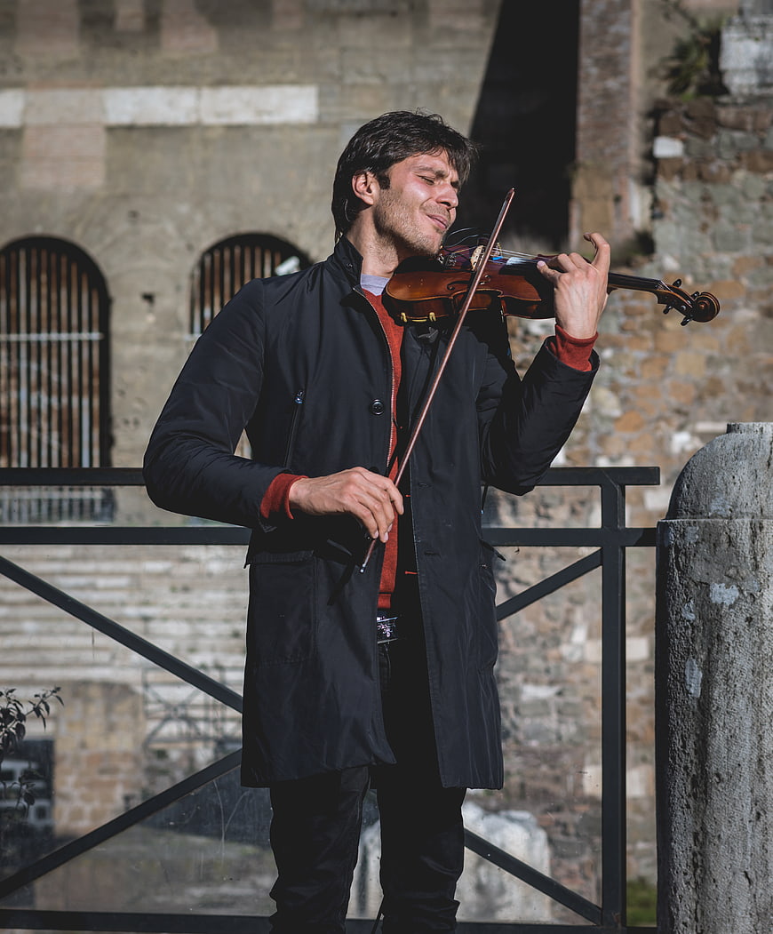 Man playing violin outdoors against historic stone ruins
