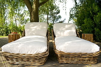 Two wicker sun loungers with white cushions on a wooden deck