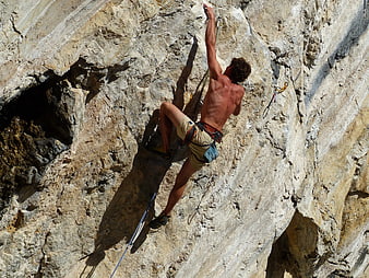 Shirtless male rock climber scaling steep limestone cliff face