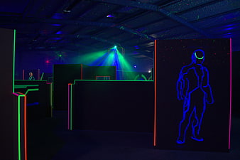 Neon-lit indoor laser tag arena with glowing player silhouette and green laser beams