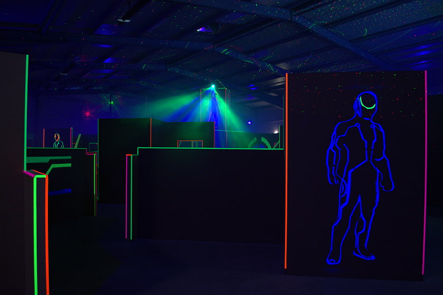 Neon-lit indoor laser tag arena with glowing player silhouette and green laser beams