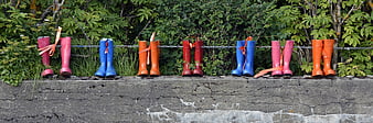 Colorful Rubber Boots Hanging on Chain Fence Against Green Foliage