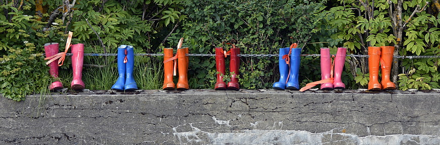 Colorful Rubber Boots Hanging on Chain Fence Against Green Foliage
