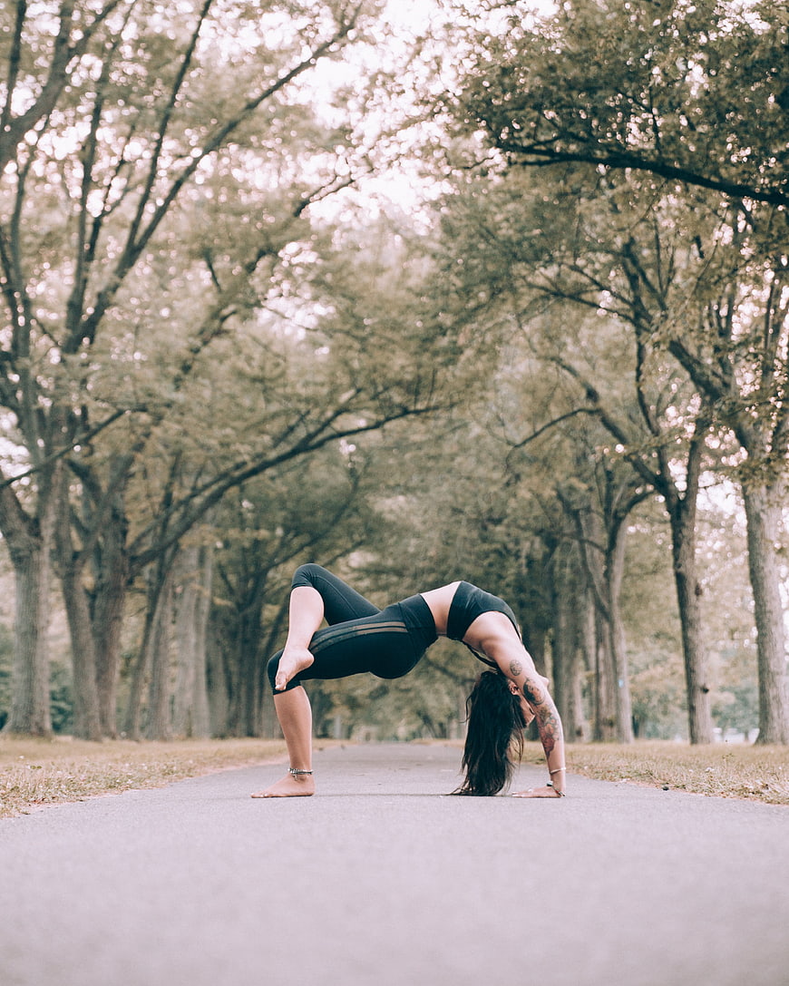 Woman performing yoga wheel pose on a tree-lined path